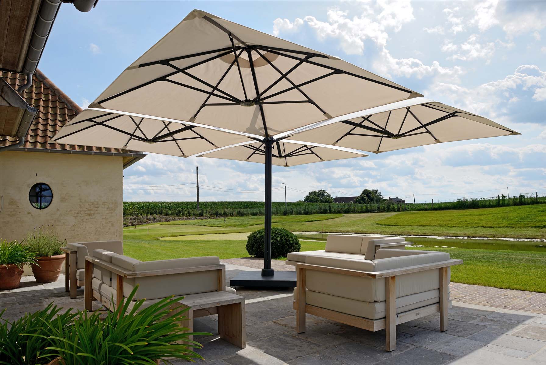 Parasol van het merk Prostor, beige van kleur, staat op een terras met uitzicht over velden, ideale zonwering buiten